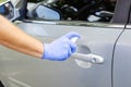 Man sanitizing door handle of his car outdoors. Male hand in protective glove holding sanitizer closeup