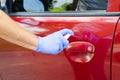Man sanitizing door handle of his car outdoors. Male hand in protective glove holding sanitizer closeup