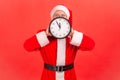 Man in santa claus hat holding wall clock near face, five minutes to midnight, new year celebration Royalty Free Stock Photo