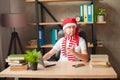 A man in a Santa Claus hat in an office behind a stack of folders and a laptop. New Year and Christmas holidays at work. Male free