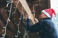 Man with santa hat decorating house outdoor carport with christmas string lights Royalty Free Stock Photo