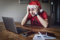 A man with a santa hat with his hands on his head in shock, using a laptop with passports, cellphone, covid digital certificates