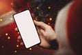 Man with santa hat holding mobile phone in hand with blank screen on christmas decorations background. online gift shopping and Royalty Free Stock Photo