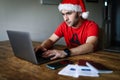 A man with a santa hat using a laptop with passports, a cellphone and covid digital certificates lying on the table