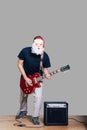 Man in Santa mask and casual clothing playing electric guitar isolated on grey background. Masked Musician playing the guitar Royalty Free Stock Photo