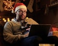 A man in Santa`s New Year hat holds a cat and working with laptop. Royalty Free Stock Photo