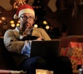 A man in Santa`s New Year hat holds a cat and working with laptop. Royalty Free Stock Photo