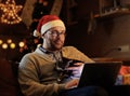A man in Santa`s New Year hat holds a cat and working with laptop. Royalty Free Stock Photo