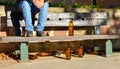 man sat on a bench with many big orange bottles of beer made of glass completely empty at the park due to somebody has drunk time