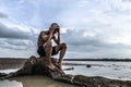 A man sat bent his knees and put his hands on his head, on the base of the tree and surrounded by water Royalty Free Stock Photo