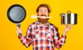 Man with saucepan and frying pan in hands. Bearded chef with wooden spoon in mouth. Cooking utensil.