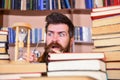 Man, scientist looks at hourglass. Teacher or student with beard studying in library. Man on serious and shocked face Royalty Free Stock Photo