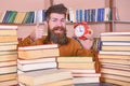 Man, scientist peeking out of piles of books with alarm clock. Teacher with beard studying in library. Time flow concept