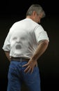 Man with screaming backache with wincing face pushing through his shirt where the pain is radiating from