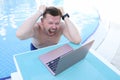 Man screaming and holding his hair and looking at laptop screen on side of pool Royalty Free Stock Photo