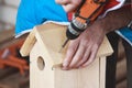 A man screws a screwdriver into the roof of a birdhouse with a cordless drill. Hands close up. DIY concept. The process of the