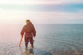 Man searching for a precious metal using a metal detector. Sea and sky on the background. Light from the left side