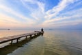 Man seated on a wooden jetty, pier looking a blue sky with cloud, silhouette reflected on the calm water. Beautiful lake. Summer