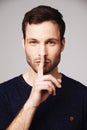 Man, secret and portrait with silence, hand and finger emoji sign in a studio. Isolated, gossip and whisper of a young Royalty Free Stock Photo