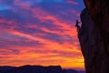 A man is seen scaling the side of a mountain during a sunset, A colorful sunset over a tall, challenging cliff-face with a lone Royalty Free Stock Photo