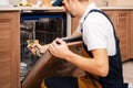 A man or a service worker in special clothing uses a screwdriver to fasten to neighboring cabinets or dismantle the dishwasher