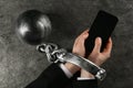 Man shackled with ball and chain holding smartphone at grey table, top view. Internet addiction