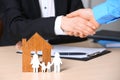 Man shaking hands with real estate agent at table, focus on family and house figures. Royalty Free Stock Photo