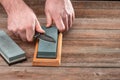 Man sharpening his pocket knife with a whetstone on a rustic wooden table