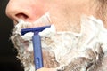 A man shaves his beard with a blue disposable safety razor. White shaving foam on the cheeks and chin Royalty Free Stock Photo