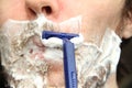 A man shaves his beard with a blue disposable safety razor. White shaving foam on the cheeks and chin Royalty Free Stock Photo