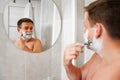 A man shaves his face with a safety razor and looks in a round mirror. Royalty Free Stock Photo