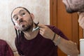 Man shaving his beard with a razor in front of the mirror. Reflection of young man shaving his beard in the mirror.