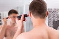 Man shaving his ear with trimmer in the bathroom Royalty Free Stock Photo