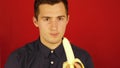 A man in a shirt cleans and eats a banana on a red background