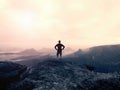 Man in shirt and jeans on the peak of sandstone rock watching into the misty and foggy valley. Beautiful moment, miracle of nature