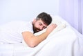 Man in shirt laying on bed, white wall on background. Guy on calm face sleeping on white sheets and pillow. Macho with Royalty Free Stock Photo