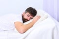 Man in shirt laying on bed, white wall on background. Nap and siesta concept. Macho with beard and mustache sleeping Royalty Free Stock Photo