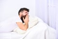 Man in shirt yawning while laying on bed, white wall and curtain on background. Sleepyhead concept. Guy on sleepy tired