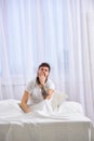 Man in shirt yawning while sit on bed, white curtain on background. Macho with beard and mustache yawning, relaxing