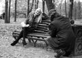 A man shooting young attractive woman sitting on the bench in autumn park, black and white photo. Royalty Free Stock Photo