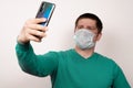 A man in a medical mask takes pictures of himself on his phone