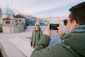 Man shoots woman with a smartphone on the pier near the Church of Our Lady of the Rocks. Back view. Montenegro