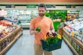 Man with shopping basket full of vegetables and fruits. Middle aged millennial man in a food store. Supermarket shopping Royalty Free Stock Photo