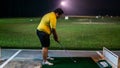 A man with a short pants holding a golf club playing at the golf driving range on a green carpet mat during the night Royalty Free Stock Photo