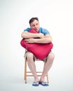Man in shorts and a t-shirt with a red suitcase sits on a chair waiting
