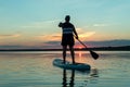 A man in shorts and a T-shirt on a SUP board with an oar against the backdrop of the sunset sky swim in the lake. Royalty Free Stock Photo