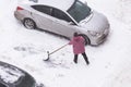 Man shoveling snow after snowfall on road, parking near car