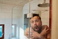 Man in the shower under cold water, freezes and hugs himself. Concept of savings and energy crisis. Royalty Free Stock Photo