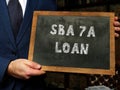 Man showing black chalkboard with written text Small Business Administration SBA 7A LOAN . Blurred background. Horizontal mockup Royalty Free Stock Photo