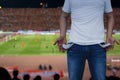 Man showing his empty pockets on blurred soccer stadium